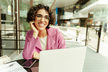 Obraz premium Happy stylish middle eastern woman in eyeglasses looking at camera using laptop