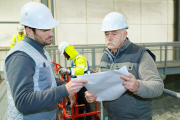 senior engineer and colleague looking at papers in factory