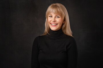 Confident blond haired woman wearing black turtleneck sweater against dark background