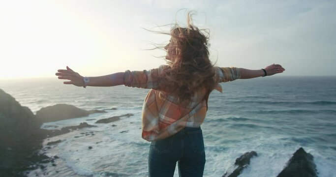 Young carefree woman spread arms as sign of happiness, accomplishment and success. Free and youthful young soul. Woman enjoy ocean breeze on edge of cliff in epic scenery