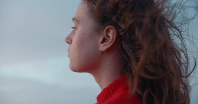 Portrait of young beautiful woman look pensive into distance. Strong ocean breeze or sea wind blow her hair. Free and youthful new generation. Cinematic real people, empowered woman 