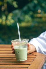 Iced matcha latte in a plastic cup in hands of a woman.