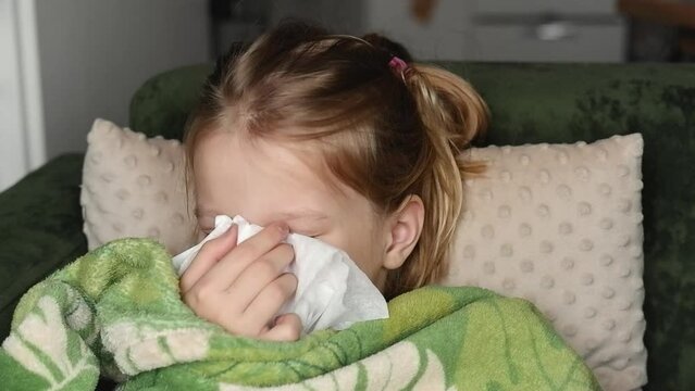 sick teenage girl sneezing in bed, has a cold, lies on a green sofa, holds a handkerchief to her nose, wrapped in a blanket