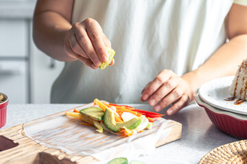 Woman preparing spring rolls in rice paper on kitchen table.