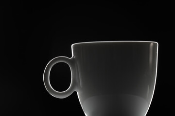 Porcelain coffee cup on a saucer isolated on black background. Close up. Dark backlit studio scene.