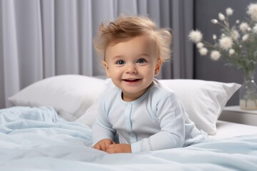 Cute newborn boy in a white cloth lying in a bed in a bright bedroom. Happy baby under blanket