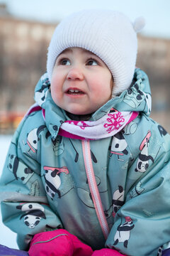 Girl with frozen red cheeks, in a hat, scarf, mittens and warm overalls