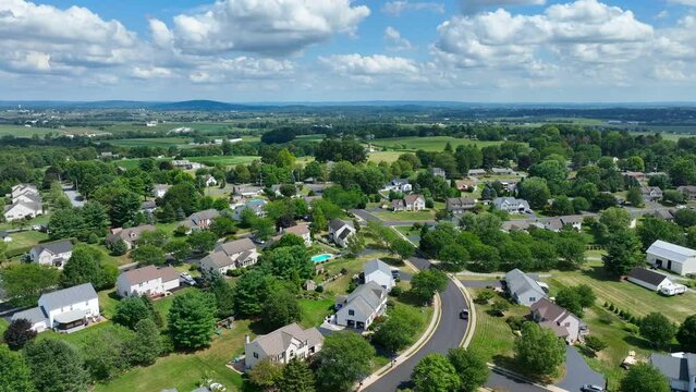 High aerial shot of American neighborhood on summer afternoon. Large houses and homes. Blue sky with puffy clouds.