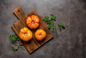 Fresh yellow tomatoes on a wooden cutting board with parsley, dark rustic background. Top view, flat lay, copy space.