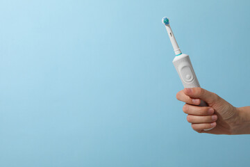 Electric toothbrush in hand on blue background