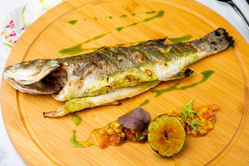 baked fish with spices and lemon on a wooden tray side view