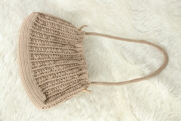 Knitted handmade milky brown bag on furry white blanket. Top view. 