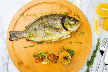 baked fish with spices and lemon on a wooden tray top view