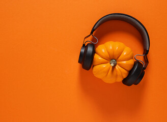 Halloween party concept. Autumn pumpkin wearing a black wireless headphone on orange colored...