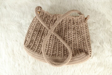 Knitted handmade milky brown bag on furry white blanket. Top view. 