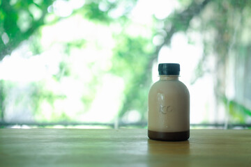 Tasty fresh milk and cocoa in plastic bottle on wood table against nature background