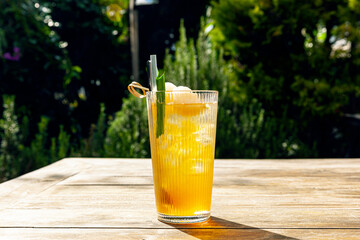 Fresh homemade Lychee ice tea with pandan leaves served on wooden table outdoors. summer cold fruit drink in sunny afternoon with green garden behind