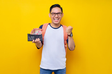 Smiling young Asian student man in casual clothes and glasses backpack holding wallet full of cash...