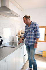 Full length portrait of a handsome Caucasian man in casual clothes switching on an electric stove in the home kitchen