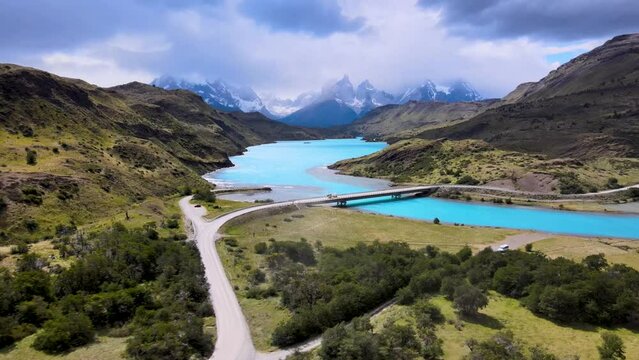 Drone flight in Patagonia, Chile and Argentina, with views of crystal blue waters and snow covered mountains and a bridge connecting mountain landscapes.