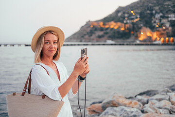 Naklejka premium Woman white dress and straw hat taking a picture with her smartphone of a view in Alanya 