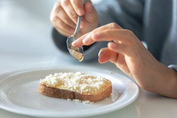 A woman sprinkles a piece of bread with grated cheese.