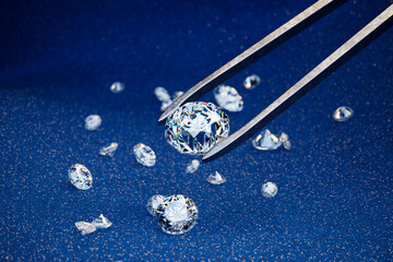 Picking one diamond with a pair of gemstone tweezers. Diamonds on a blue fabric.