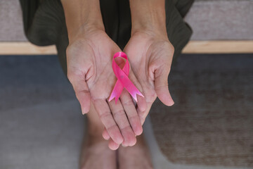 Close-up woman hand holding pink ribbon symbol. Breast cancer awareness and october pink day, world cancer day, national cancer survivor day. healthcare concept