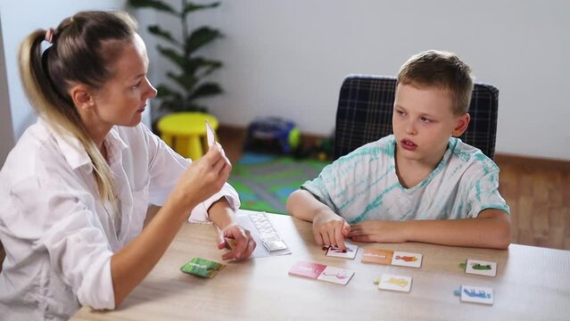 ABA Therapist Leads Therapy Session with Autistic Boy Using Color Cards; Rewards with Tokens; Bright Room with White Walls, Wooden Floor; Fiddle Leaf Fig (Ficus Lyrata) & Toys in the Background