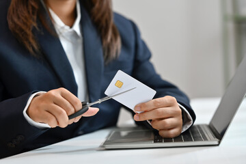 Woman cutting credit card with scissors at her workplace. Bankruptcy, financial problems concept