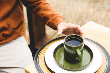 A man takes a cup of coffee or other hot beverage sitting at the breakfast table, without a face