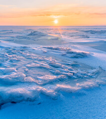 Winter landscape. Snowdrifts on the ice surface during sunset.