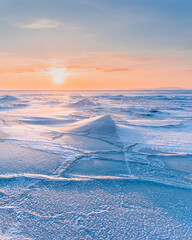 Winter landscape. A frozen surface of ice with snow intersected by many cracks.