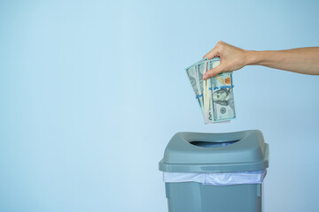 Female put money dollar into trash basket. Inflation concept money in a trash can