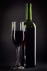 bottle and glass of red wine on a black background with copy space