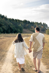 A man and a woman walk into a field holding hands.