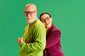 Love and support. Caring, elegant senior couple, man and woman in casual clothes posing together against green studio background. Concept of beauty and fashion, relationship, modern style, age