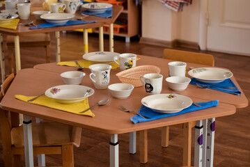 Lunch in kindergarten, on a small table are plates. Meal time in kindergarten. Dining room the wooden chairs and small tables