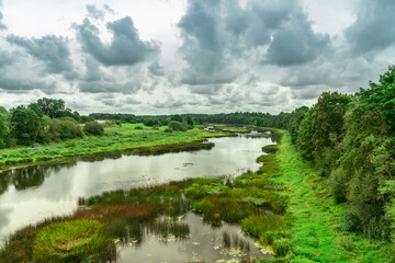 Rural landscape with river, reeds, forest and blue cloudy sky