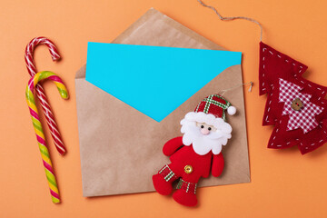 Top view of a mail envelope with a blank sheet and various Christmas decorations on a colored background, a template for a designer on the theme of letters to Santa Claus