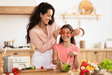 Joyful mom and kid making salad having fun in kitchen