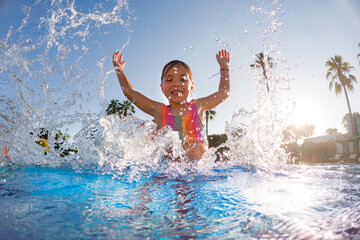 Little girl splashing water in the pool, playing in the water, having fun. Beach resort vacation by...