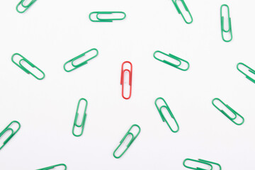 Red paperclip with multiple green paperclip on white background, unique concept