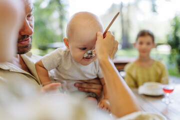 A small baby is being fed soup with big spoon. The mother feeding young child in a restaurant.