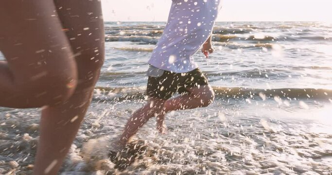 A Woman and a Child Run through the Water, they are doused by Waves and Spray flying in different directions, Slow motion. Fun on the Beach at Sunset. Vacation at Sea.