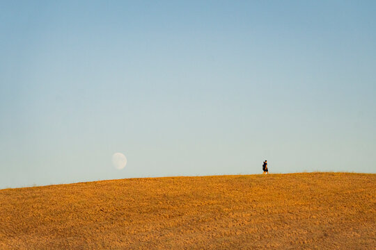 coppia passeggia su collina con dietro enorme luna crescente