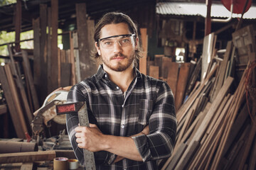 Portrait of Caucasian male carpenter wearing safety glasses and holding woodworking tool at woodwork workshop studio with background of lumber. copy space