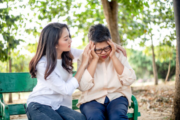Asian young daughter worried of sick mother suffering from headache flu or fever disease at park....