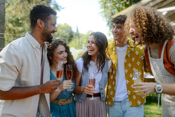 Friends and family talking and having fun at summer grill garden party. People at party laughing, holding glasses with drinks.