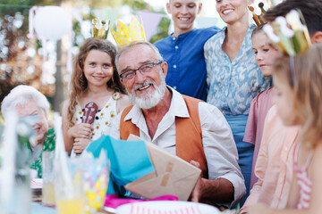 Family birthday garden party for senior man. Family sitting at table having fun, girl playing ukulele for the birthday man.